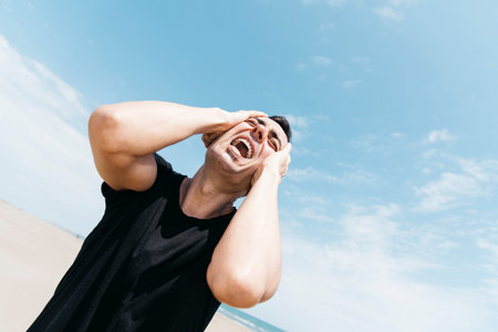 closeup of a suffering caucasian man outdoors, screaming with his hand in his head