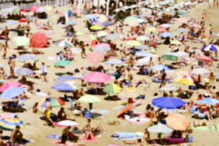 a defocused blur background of a packed beach, with many umbrellas of different colors, in summerの写真素材