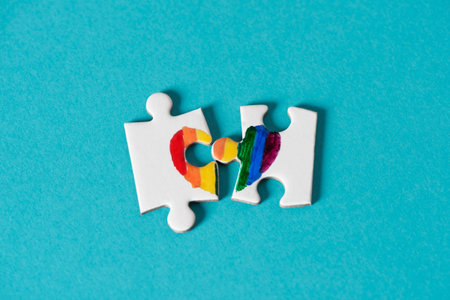 two pieces of a puzzle, which put together form a rainbow heart, on a blue background, depicting the...