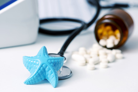 closeup of a blue plastic starfish and some pills on a doctors desk, in a doctors office, depicting the medical assistance in summerの写真素材