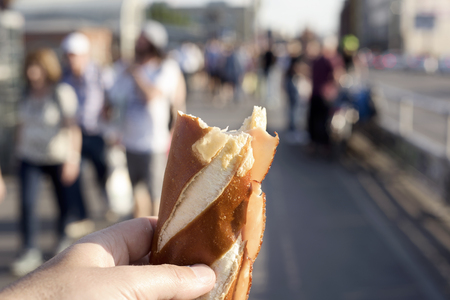 closeup of a caucasian man eating a sandwich, made with a german Laugenstange roll, in an outdoors train or tram stationの写真素材