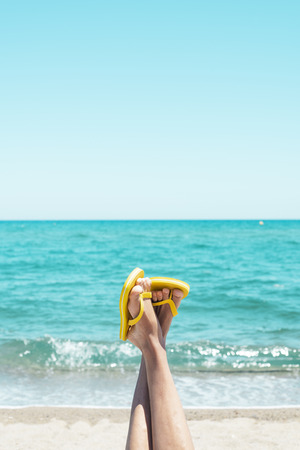 closeup of the legs of a young caucasian man on the beach, upside down, wearing a pair of yellow flip-flops, against the sky with a blank space on topの写真素材