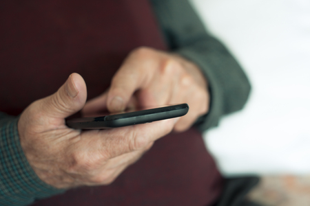 closeup of an old caucasian man sitting in a couch using a smartphoneの写真素材