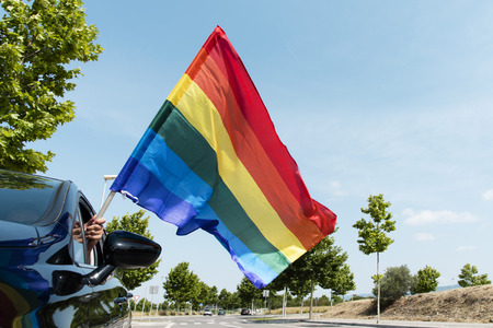closeup of a young caucasian man waving a rainbow flag by the window of a carの写真素材