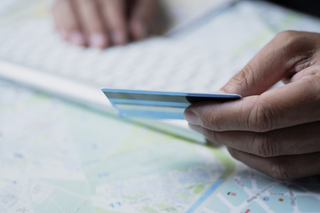 closeup of a caucasian man using a credit card to book a trip online, using his computer, on a table full of mapsの写真素材