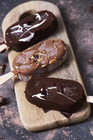 high angle view of some chocolate ice cream bars on a chopping board, placed on a dark rustic wooden tableの写真素材