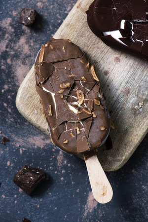 high angle view of some chocolate ice cream bars on a wooden cutting board, placed on a dark rustic wooden table sprinkled with cocoa powderの写真素材