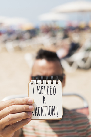 closeup of a young caucasian man on the beach showing a spiral notepad with the text I needed a vacation handwritten in the first pageの写真素材