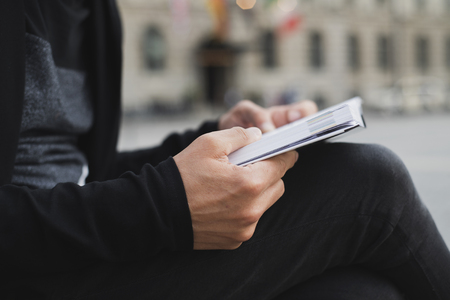closeup of a young caucasian man, in casual wear, reading a book, sitting in a bench on the streetの写真素材