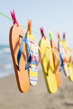 closeup of some different pairs of colorful flip-flops hanging on a clothes line on the beach, with the sea in te backgroundの写真素材