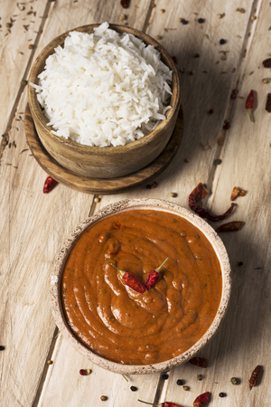high angle view of a bowl with a chicken korma curry and a bowl with cooked rice on an off-white wooden tableの写真素材