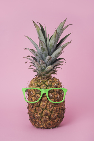 closeup of a pineapple wearing a pair of neon green lensless glasses on a pink backgroundの写真素材