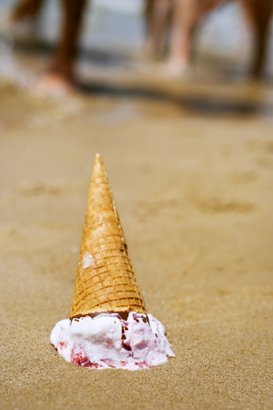 closeup of an ice cream cone upside down dropped on the sand of a beachの写真素材