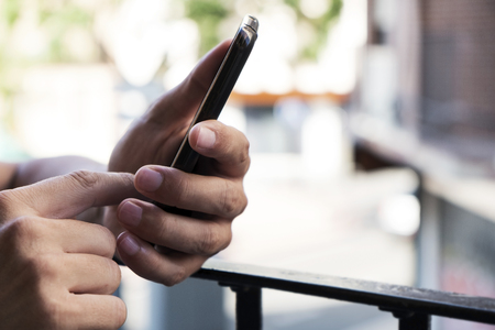 closeup of a young caucasian man using his smartphone in the balcony of his home or of a hotel room in a cityの写真素材