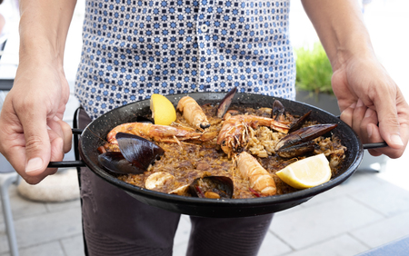 closeup of a young caucasian holding a typical spanish seafood paella in the paellera, the paella panの写真素材