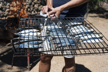 closeup of a young caucasian man about to grill some raw sardines on a bonfire outdoorsの写真素材