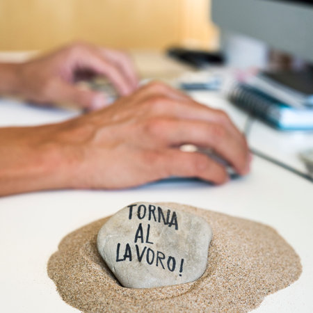 closeup of a man sitting at his office desk, and stone on a pile of sand in the foreground with the...