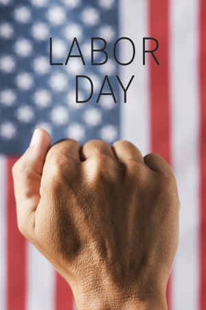 closeup of the raised fist of a young man and the text labor day against a flag of the United Statesの写真素材