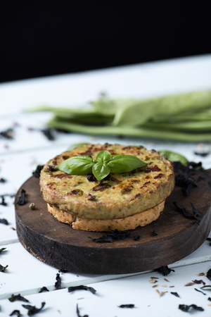 closeup of some veggie burgers, made with green beans and other vegetables, on a round wooden tray, placed on a pale green rustic wooden tableの写真素材