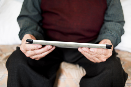 closeup of an old caucasian man sitting in a couch using a tablet or an e-readerの写真素材