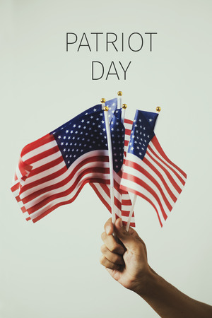 closeup of a young caucasian man with some american flags in his hand and the text patriot day, against an off-white backgroundの写真素材
