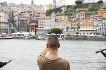 closeup of a young caucasian man, seen from behind, taking a picture of the Douro River and Porto, in Portugal, with his smartphone, from Vila Nova de Gaiaの写真素材
