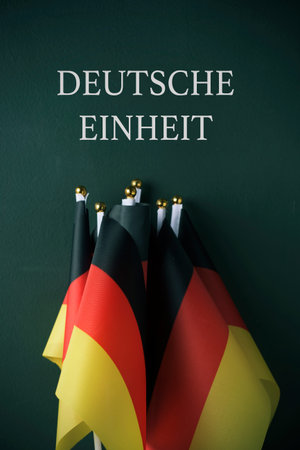some flags of Germany and the text Deutsche Einheit, German Unity written in German, against a dark green background