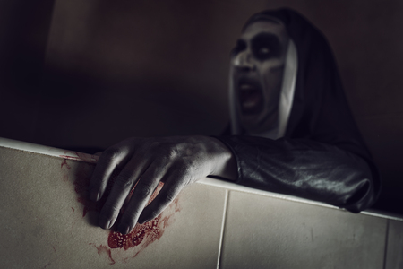 Closeup of a frightening evil nun, wearing a typical black and white habit, with her hands stained with bloodの写真素材
