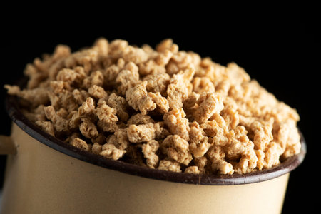 closeup of an old beige enamelware pot full of chunks of textured soy protein, against a black...