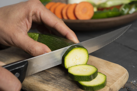 Closeup of a caucasian man cutting a zucchini into slices with a knifeの写真素材