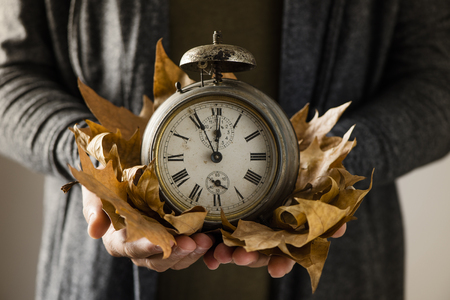 Closeup of a young man with an old and rusty alarm clock surrounded by dry leaves in his handsの写真素材