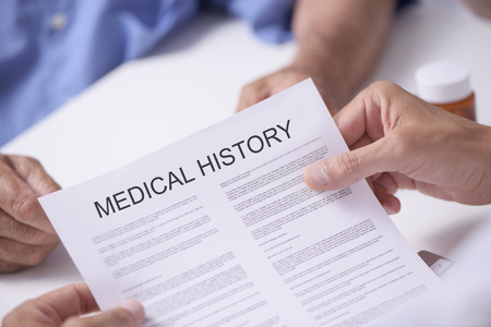 Closeup of a caucasian doctor man reading the medical history of a senior caucasian patient manの写真素材