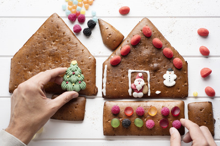 High angle view of a young Caucasian man making a homemade gingerbread house, on a white tableの写真素材