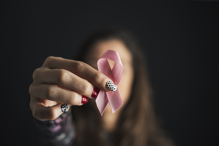 Closeup of a young caucasian woman holding a pink ribbon in front of her face, for the breast cancer awarenessの写真素材