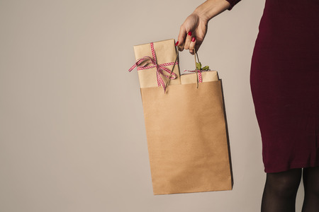 Closeup of a young caucasian woman holding a paper shopping bag full of gifts against an off-whiteの写真素材