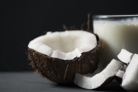 Closeup of some pieces of coconut and a glass of coconut milk on a gray rustic wooden table, against a blackの写真素材