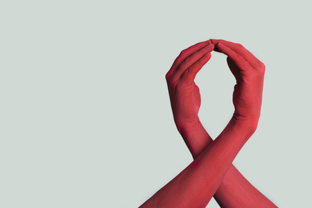 closeup of the arms of two men painted red forming a red awareness ribbon for the fight against AIDS, against an off-white background with some blank space on the leftの写真素材