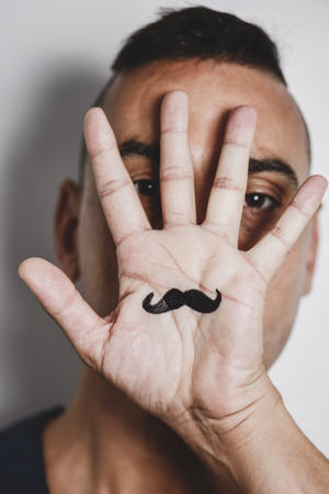 closeup of a young caucasian man with the palm of his hand in front of his face, with a mustache drawn in itの写真素材