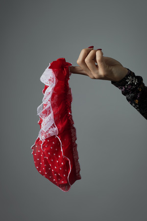 closeup of a young woman with a pair of red panties in her hand, against a gray backgroundの写真素材