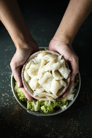 high angle view of a young caucasian man about to prepare xato, a catalan salad with desalinated salt cod and escarole endive, on a rustic dark green tableの写真素材