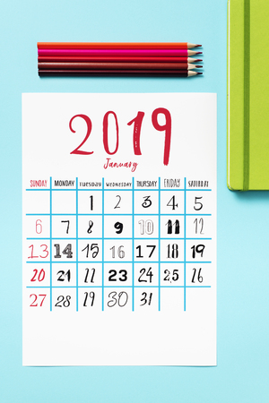high angle view of a calendar of 2019 on a blue table, next to some pencil crayons of different colors and a green notepadの写真素材