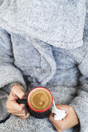 High angle view of an ill young Caucasian man at home wearing a fluffy house robe with a hoodの写真素材