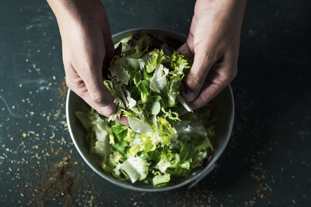 Closeup of a young Caucasian man about to prepare a salad with a mix of different salad leavesの写真素材