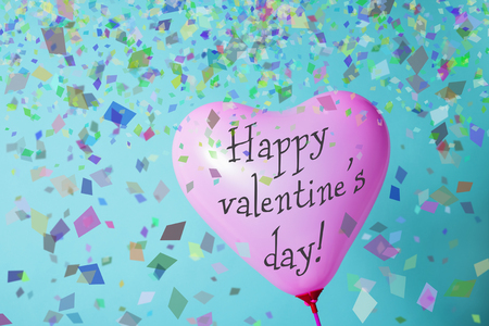 a pink heart-shaped balloon with the text happy valentines day and some confetti against a blue backgroundの写真素材