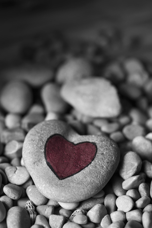 closeup of a stone with a red heart painted on it, on a pile of smaller stonesの写真素材