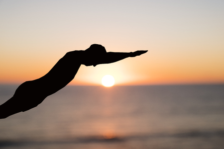 Closeup of a black paper cutout in the shape of a man throwing himself into the ocean, at dawn or at sunsetの写真素材