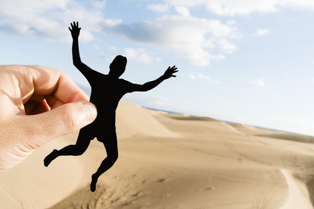Closeup of the hand of a caucasian man holding a paper cutout in the shape of a young man having fun on the sand dunesの写真素材