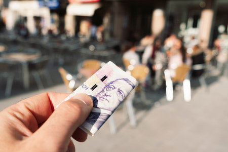 Closeup of a young caucasian man on the terrace of a cafe about to pay the bill with czech korunas...