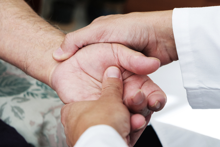 Closeup of a Caucasian man, in a white coat, moving the hand of a senior Caucasian patient man, at his home or at a nursing homeの写真素材