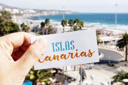 Closeup of the hand of a caucasian man holding a signboard with the text Islas Canarias, Canary Islands written in Spanish, at Playa del Ingles, in Maspalomas, Gran Canaria, Spainの写真素材